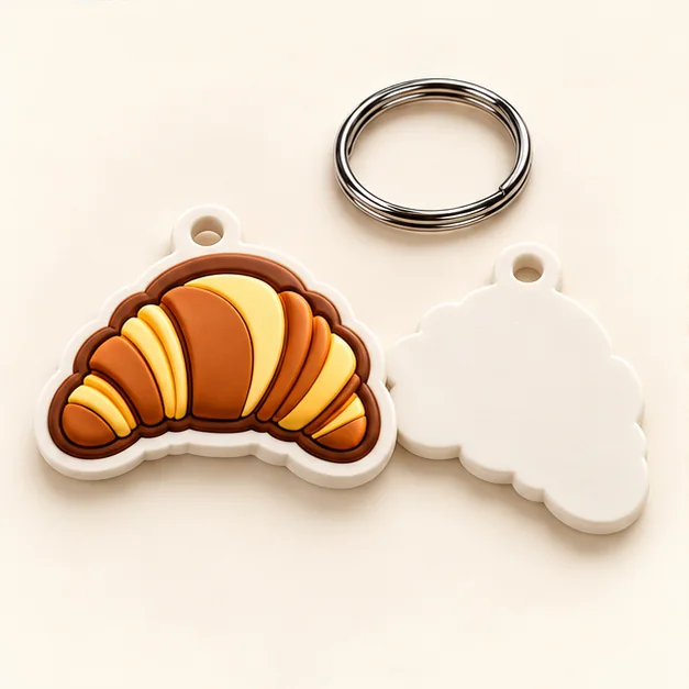 Illustrative croissant-shaped physical keychain prototype with a metal ring